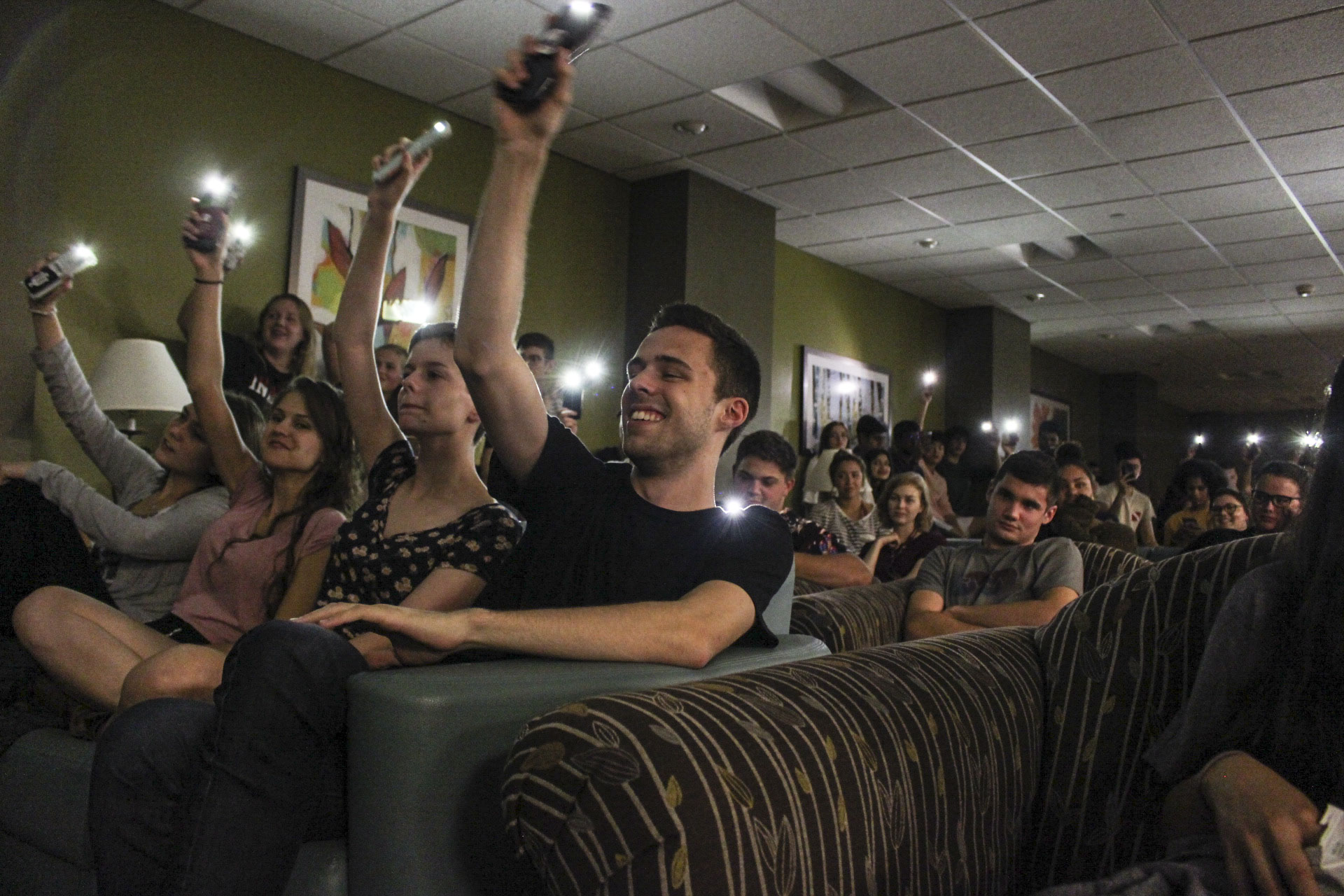 Students watching an open mic night holding their cell phones up with the flashlight on